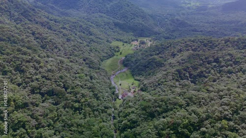 Serene river winding through green mountain valleys. Lush vegetation blankets the landscape. Peaceful flight over nature's beauty