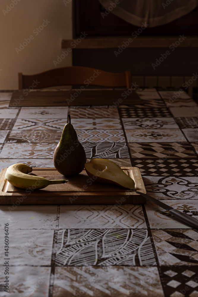 Preparing healthy fruit: Pear, banana, cut pear on wood board, knife ready. Dramatic lighting.