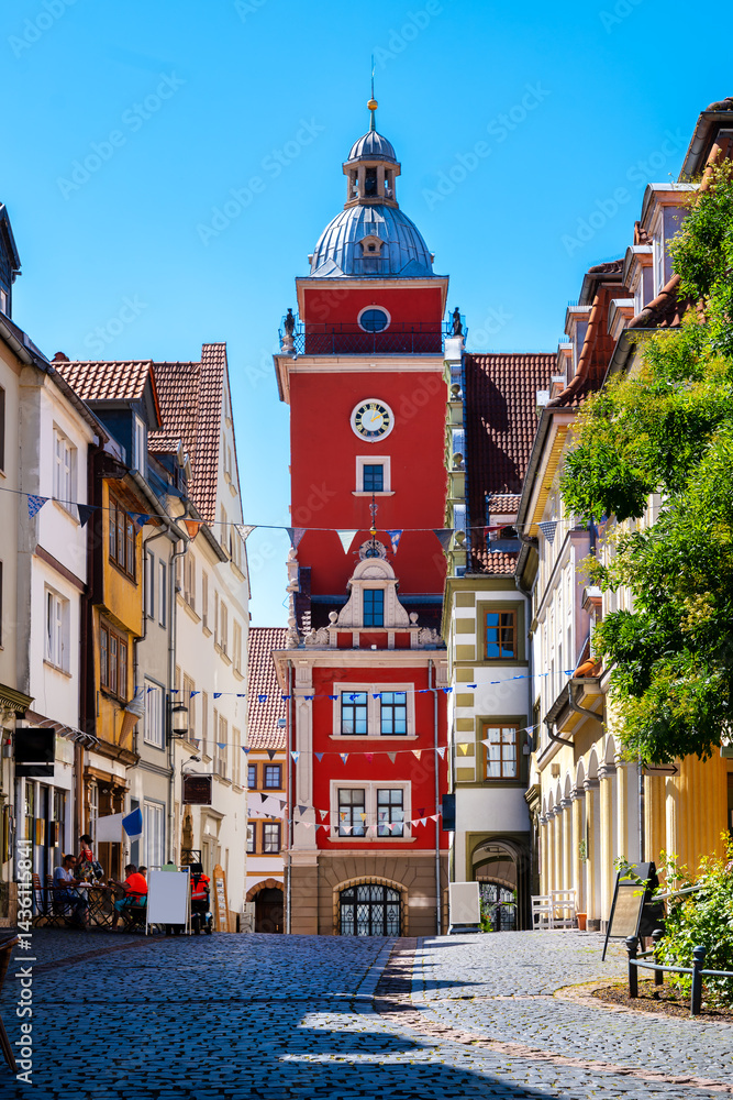 Old Town Hall Tower in Gotha framed by historic alley with flags and cobblestones under summer skies
