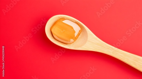 Obraz na płótnie A wooden spoon holds a glistening amber gel against a vibrant red backdrop w salonie