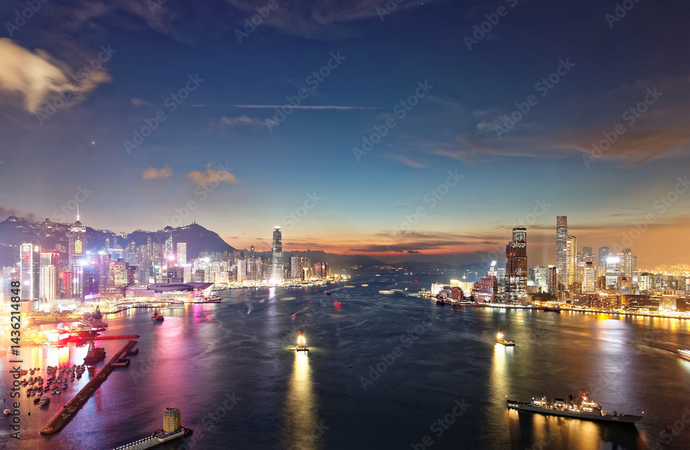 Fototapeta premium Scenery of Hong Kong at nightfall, with a city skyline of modern skyscrapers by Victoria Harbour between Kowloon & Hongkong Island and ships navigating in the busy seaport under beautiful twilight sky