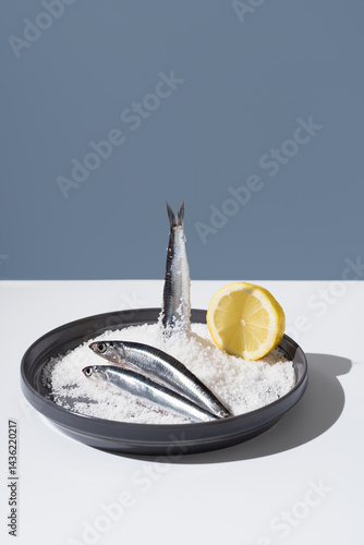 Tres anchoas frescas con limón sobre un plato lleno de sal sobre fondo azul	