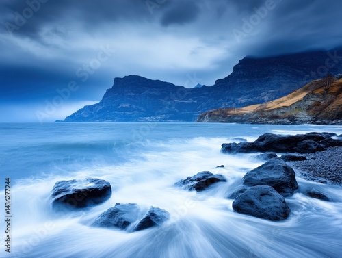 Dramatic coastal scene; moody sky over dark, rocky beach with waves
