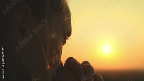girl prays looking sunset, long hair flying away in glare sunlight rays strong wind, looking at dawn, lonely hike of brave girl, looking into sky with her eyes, believing good. close-up hands face