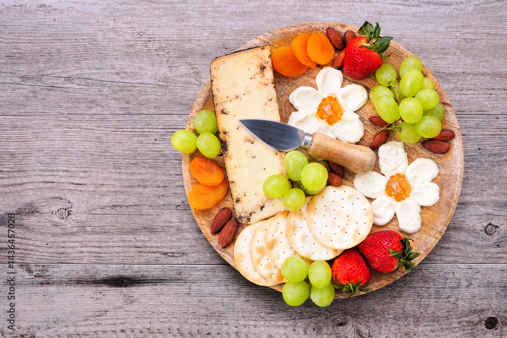 Summer theme charcuterie board against a wood background. Selection of fruits, cheeses and crackers. Top view.