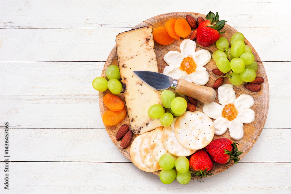 Summer theme charcuterie board against a white wood background. Variety of fruits, cheeses and crackers. Overhead view.