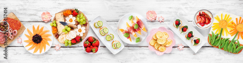 Obraz na płótnie Summer garden party food table scene. Assortment of fun flower theme charcuterie items, cheese, fruit, vegetables and finger snacks. Above view on a white wood banner background. w salonie