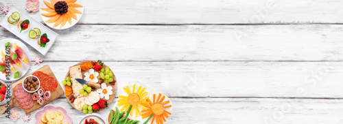 Obraz na płótnie Summer garden party food corner border. Assortment of fun flower theme charcuterie items, cheese, fruit, vegetables and finger snacks. Above view on a white wood banner background. w salonie
