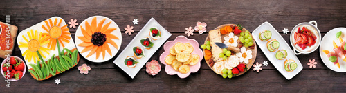 Obraz na płótnie Summer garden party food table scene. Variety of fun flower theme charcuterie items, cheese, fruit, vegetables and finger snacks. Overhead view on a dark wood banner background. w salonie