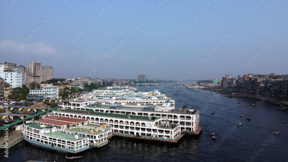 Obraz premium Dhaka is located on the banks of the Buriganga river. Aerial view of Sadar Ghat and the Buriganga river with modern cityscape and boats, Dhaka, Bangladesh.