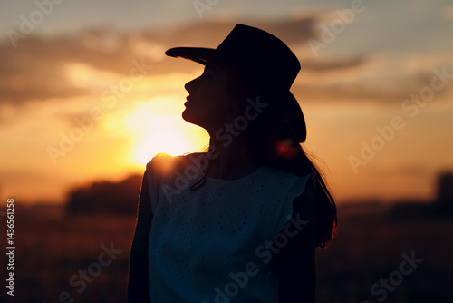 Woman farmer silhouette in cowboy hat at agricultural field on sunset.