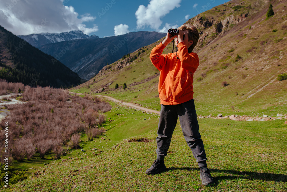 Fototapeta premium Child tourist with binoculars standing in high mountains on summer day