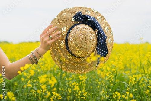 Un cappello estivo tenuto da una donna in mano in primavera nel campo di colza in Italia