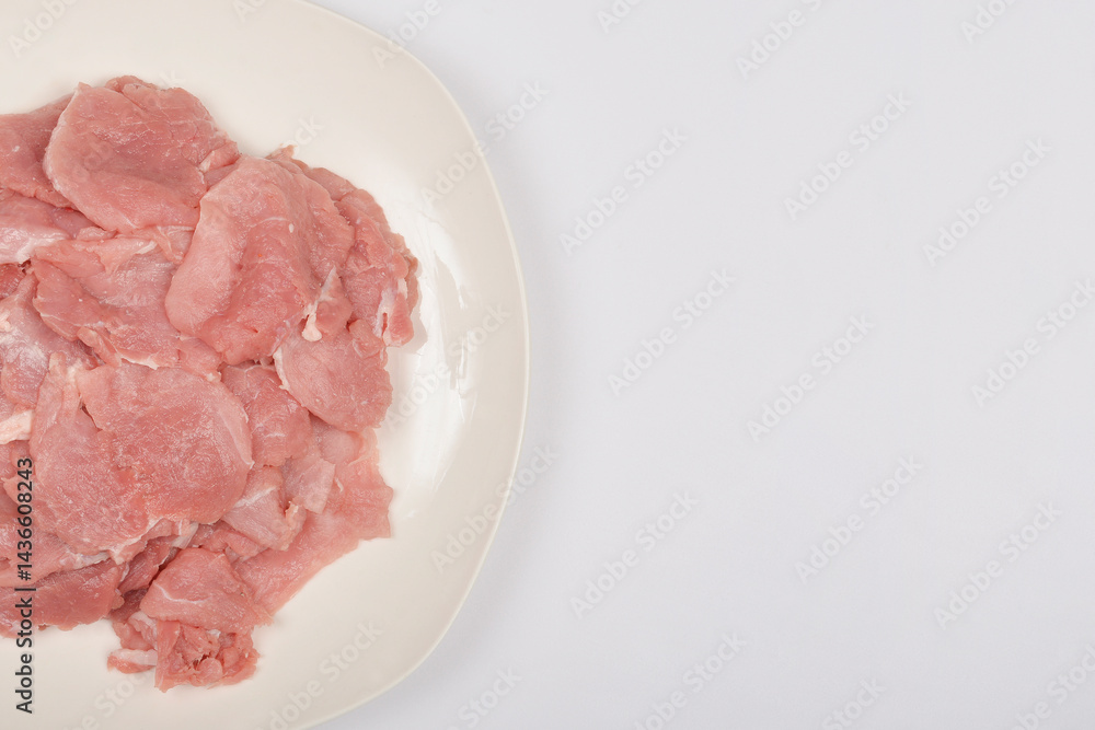 Raw pork tenderloinThinly sliced raw pork tenderloin is piled on a white plate, presented in a top-down shot on a light background