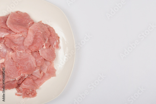 Raw pork tenderloinThinly sliced raw pork tenderloin is piled on a white plate, presented in a top-down shot on a light background