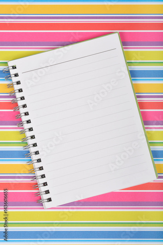 A blank, lined spiral notebook lies diagonally on a vibrant, multicolored striped background