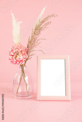 Beautiful pink picture frame mockup with a transparent blank canvas, standing on a pink table, next to flowers in a vase, pink background