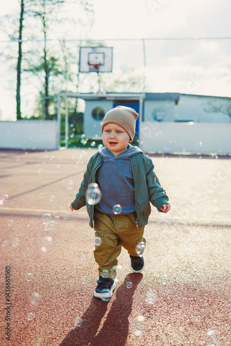 Obraz na płótnie Toddler boy running outside with soap bubbles. Child on a warm spring day for a walk in a jacket and hat. w salonie