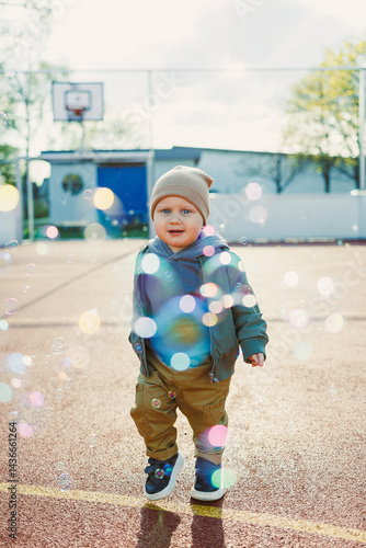Obraz na płótnie Toddler boy running outside with soap bubbles. Child on a warm spring day for a walk in a jacket and hat. w salonie