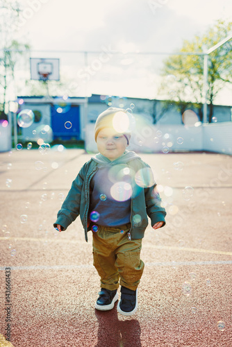 Obraz na płótnie Toddler boy running outside with soap bubbles. Child on a warm spring day for a walk in a jacket and hat. w salonie