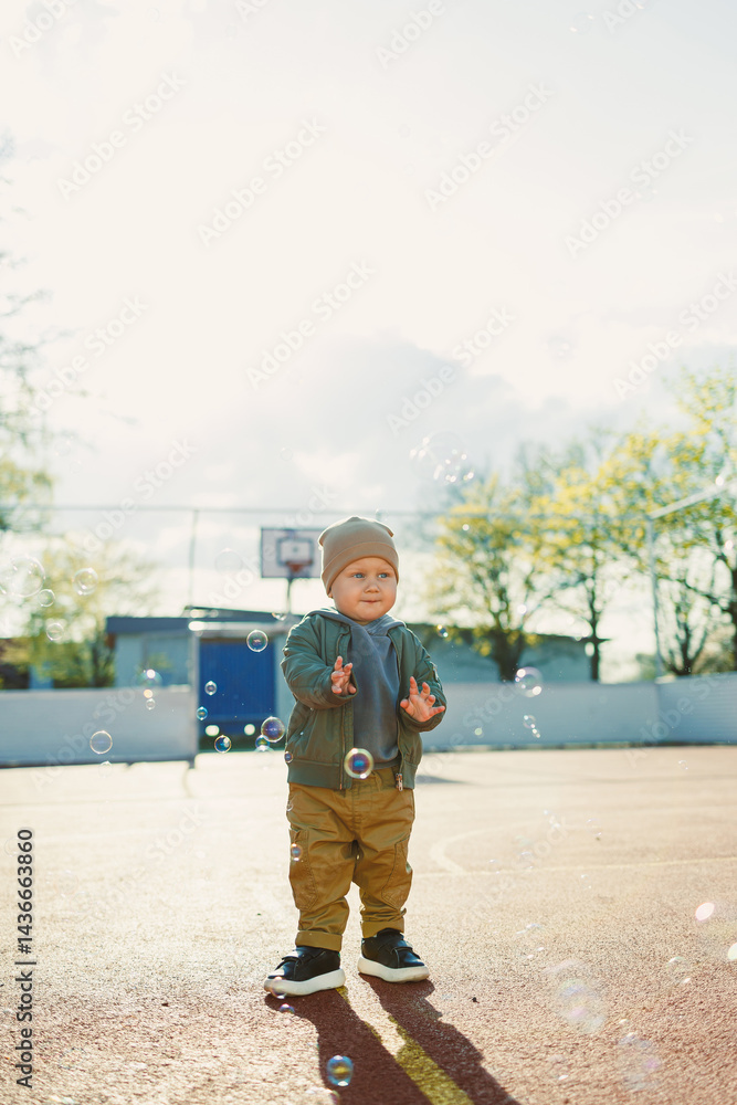 Little cute boy 2 years old running with soap bubbles. Boy catching soap bubbles in the park, enjoying a sunny summer day. Creative activities for children outdoors