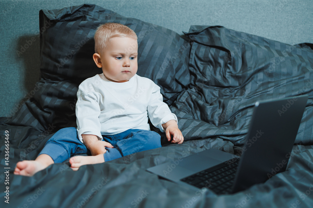 A 2-year-old boy sits in bed and presses buttons on a laptop. The child plays with a laptop.