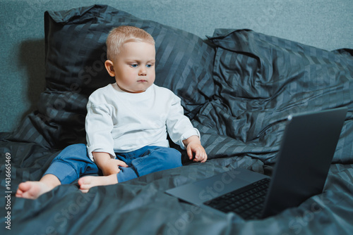 Obraz na płótnie A 2-year-old boy sits in bed and presses buttons on a laptop. The child plays with a laptop. w salonie
