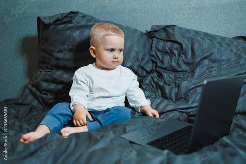 Obraz na płótnie A 2-year-old boy sits in bed and presses buttons on a laptop. The child plays with a laptop. w salonie