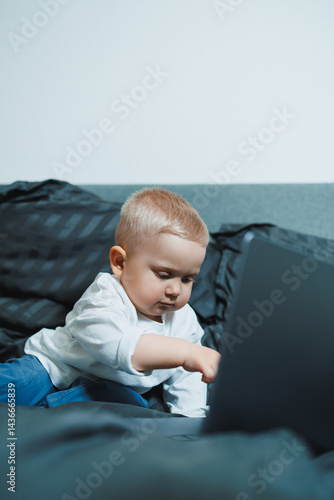 Obraz na płótnie A 2-year-old boy sits in bed and presses buttons on a laptop. The child plays with a laptop. w salonie