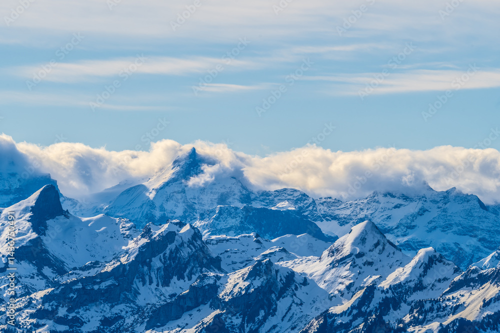 Fototapeta premium Majestic snowy mountains under a clear blue sky with wispy clouds in the distance during midday sun