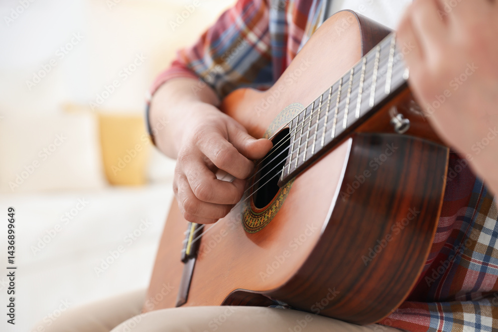 Fototapeta premium Man playing guitar at home, focus on hand