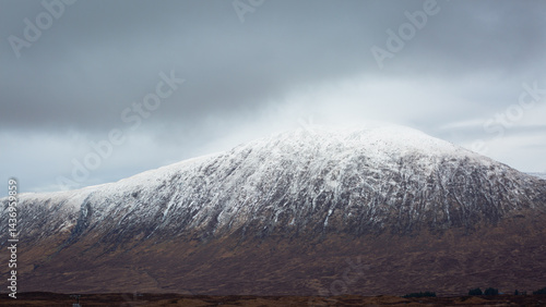 A breathtaking panoramic view of the Scottish Highlands, featuring snow-capped mountains rising above vast open moorland and rugged terrain.