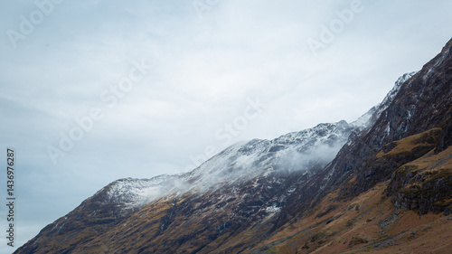 A breathtaking panoramic view of the Scottish Highlands, featuring snow-capped mountains rising above vast open moorland and rugged terrain.