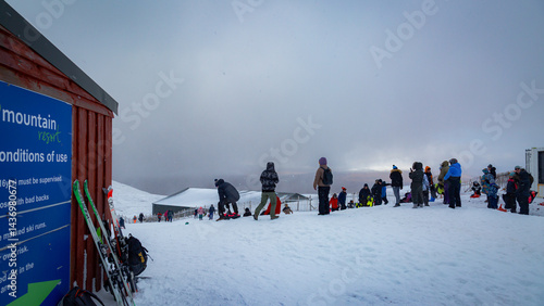 A large group of people walk together across the snow-covered slopes at Glencoe Mountain Resort in the Scottish Highlands. Dressed in winter gear, they move through challenging blizzard conditions