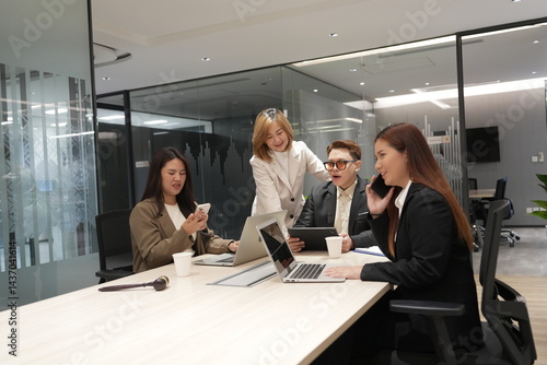 Obraz na płótnie A group of lawyers sit in a meeting to discuss and find a solution, and an Asian female lawyer holds a smartphone and talks to her clients in a meeting room at a law office. w salonie