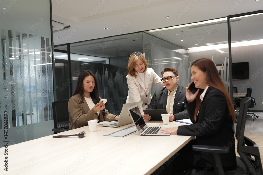A group of lawyers sit in a meeting to discuss and find a solution, and an Asian female lawyer holds a smartphone and talks to her clients in a meeting room at a law office.