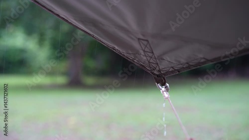 rainy season camping with heavy rain water drips droplets to tip tarp and flow motion on fly sheet tent with carabiner paracord rope umbrella by holiday travel on nature forest garden with rain sound