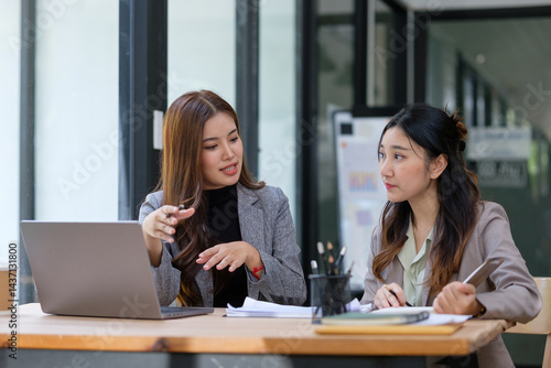 Two female professionals engaged in a serious conversation at a desk, analyzing documents and sharing ideas in a modern office setting.