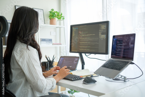Woman using external keyboard and stylus, programming across a three-screen workstation in home office.