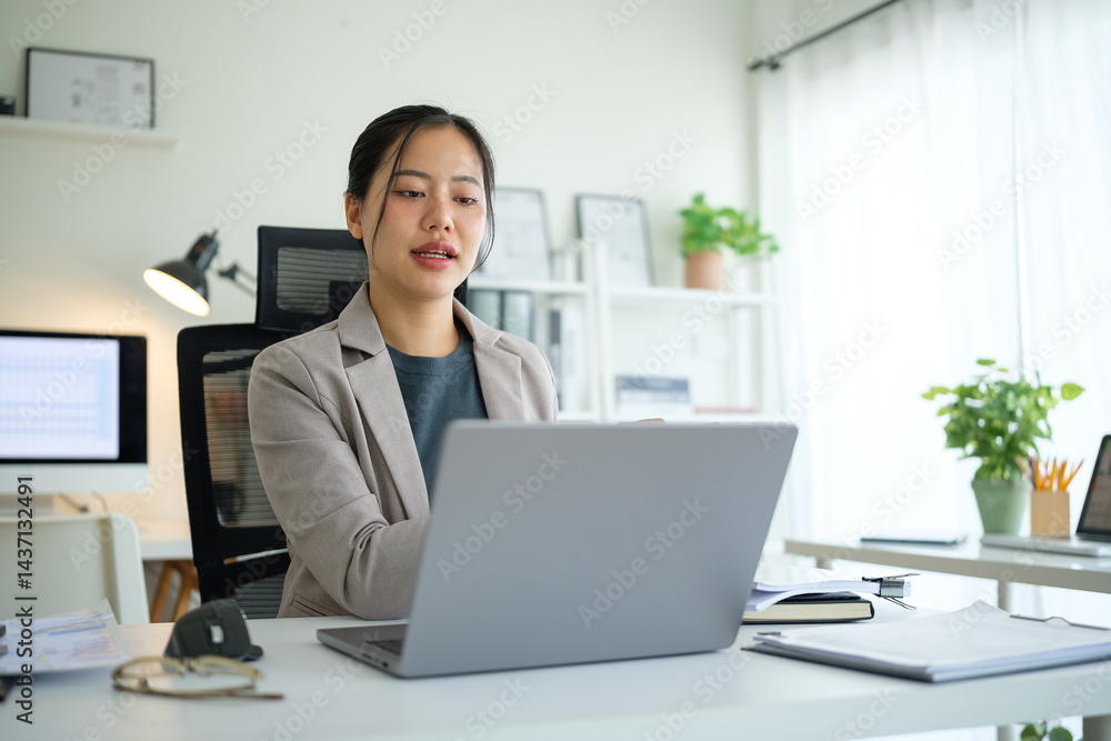 Young businesswoman in a blazer enjoying remote work, typing on a laptop at a bright desk with documents and charts. Young businesswoman in a blazer enjoying remote work, typing on a laptop at a bright desk with documents and charts.