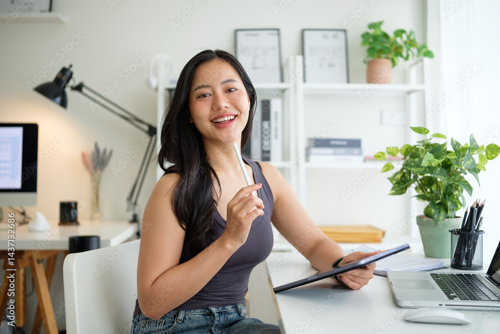 Smiling young woman holding stylus and digital tablet sitting in a bright home office. Smiling young woman holding stylus and digital tablet sitting in a bright home office.