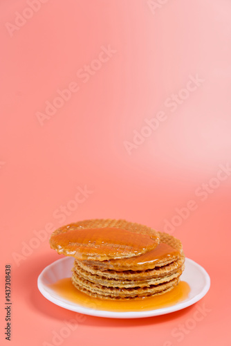 Stack of stroopwafels with melted caramel dripping on plate over pink background