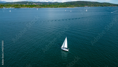 Foto Serene Sailing on the Lake: A solitary sailboat gracefully glides across a tranquil lake, with the vast expanse of water meeting the horizon in a peaceful setting