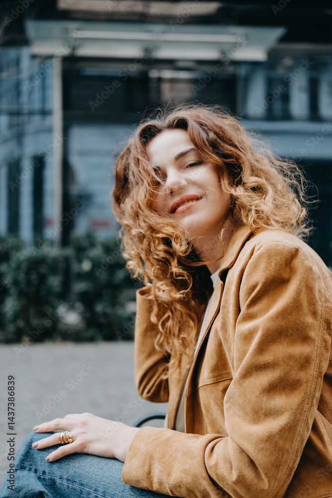 Fototapeta premium A young woman with curly red hair sits quietly on a bench looking down with a calm expression. Quiet contemplation, thoughtful mood, inner calm, soft elegance...