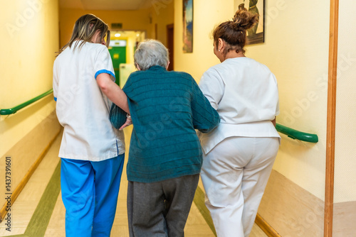 Obraz na płótnie Nurses helping elderly woman walking in nursing home corridor w salonie