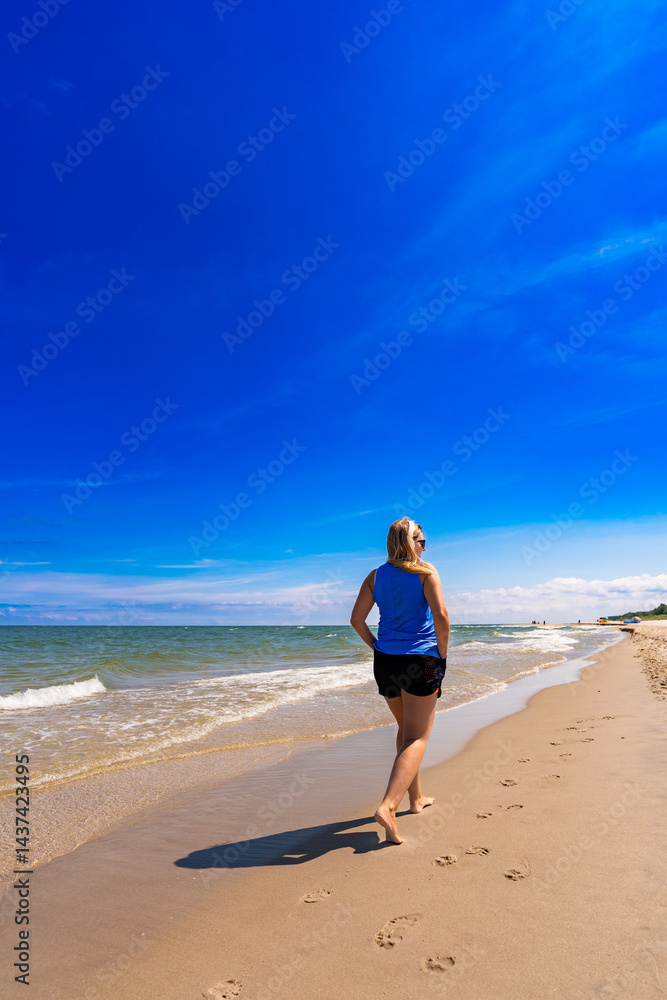 Beautiful mature woman walking on sandy beach in summertime. Back view Beautiful mature woman walking on sandy beach in summertime. Back view