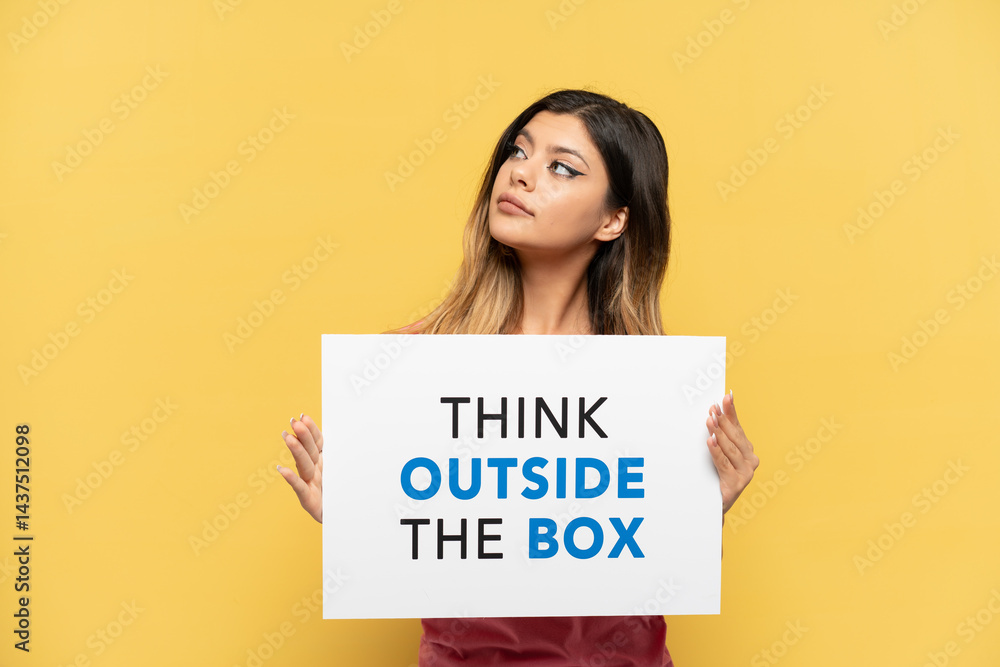 Young Russian girl isolated on yellow background holding a placard with text Think Outside The Box Young Russian girl isolated on yellow background holding a placard with text Think Outside The Box