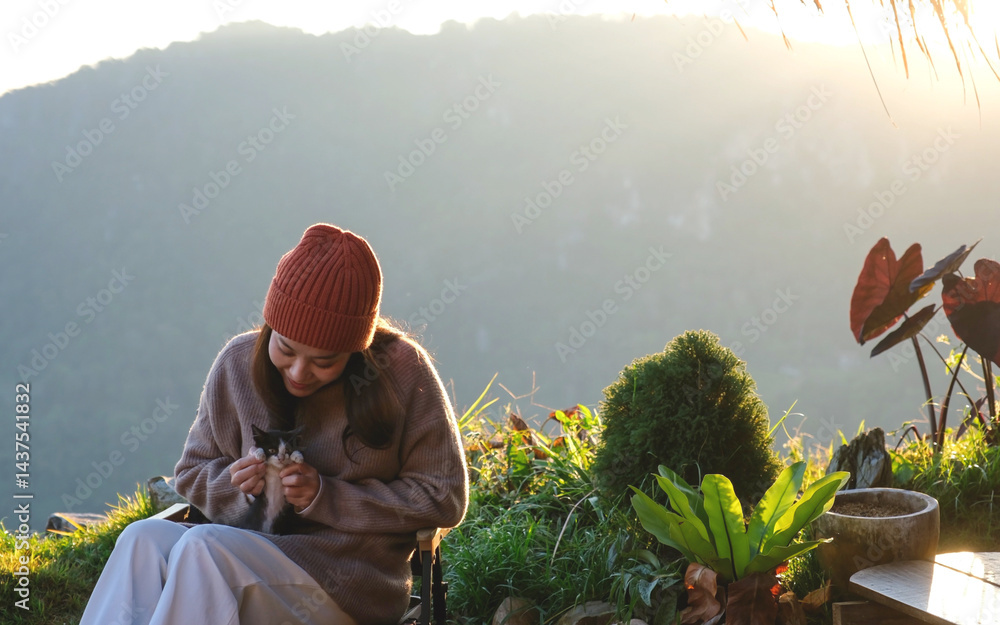 A woman holding and playing with a cat with a beautiful mountain and nature view