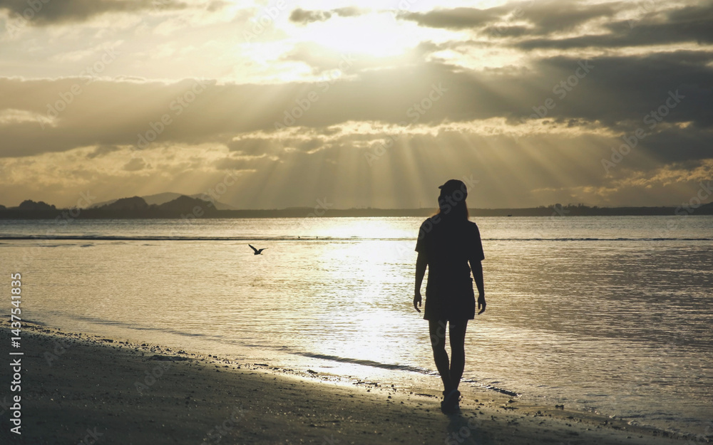 Silhouette of a woman with hat standing on the beach in the morning