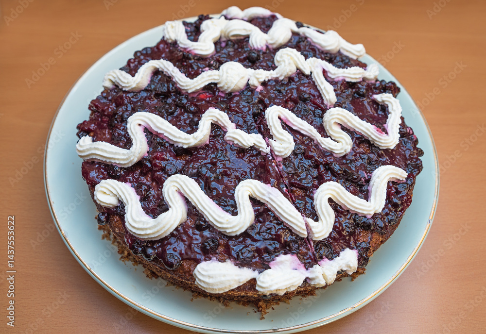 Wholemeal cake with blueberry icing and cream topping on a porcelain plate, wooden table